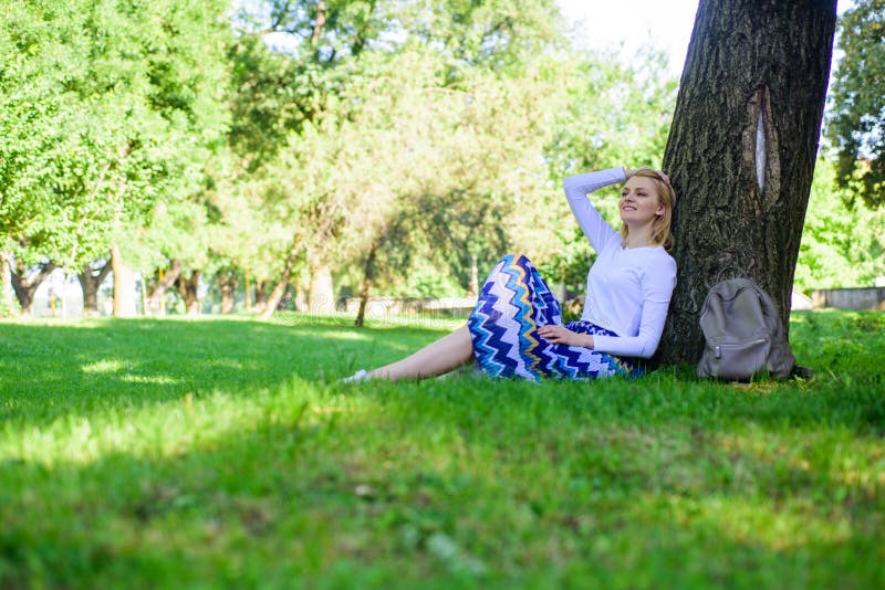Give yourself break and enjoy leisure. Find peaceful place in park. Girl sit on grass lean on tree trunk relaxing in shadow green nature background. Woman blonde take break relaxing in park. Give yourself break and enjoy leisure. Find peaceful place in park. Girl sit on grass lean on tree trunk relaxing in shadow green nature background. Woman blonde take break relaxing in park.