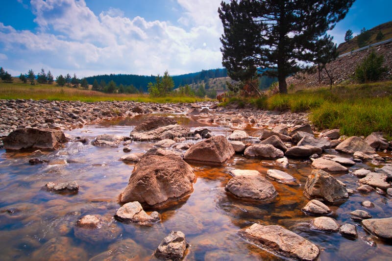 Beautiful calm mountain river Rzav on the mountain of Zlatibor, Serbia, late summer, with rock formation in foreground. Beautiful calm mountain river Rzav on the mountain of Zlatibor, Serbia, late summer, with rock formation in foreground