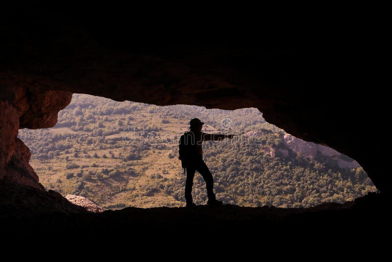Gebirgsmann mit Hut und Rucksack am Eingang einer Höhle Hervorhebung stockbild