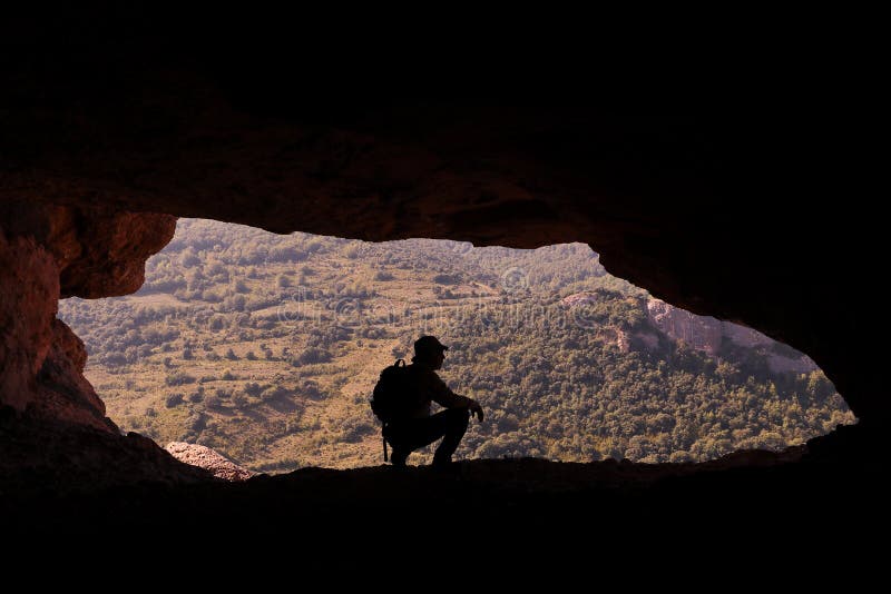 Gebirgsmann mit Rucksack und Hut duckte sich am Eingang einer Höhle lizenzfreies stockbild