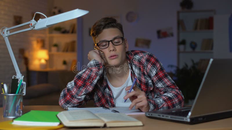 Gebohrter Student, der am Telefon mit Freund plaudert, anstatt, Zeit vergeudend zu studieren