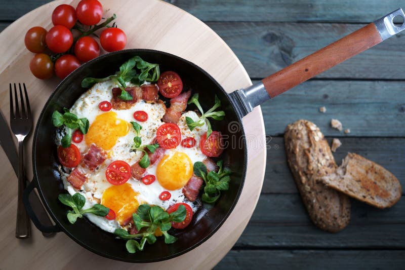 Gebraden eieren met bacontomaten en greens, gietijzer pan, hoogste mening stock fotografie Gebraden eieren met bacontomaten en greens, gietijzer pan, hoogste mening stock fotografie