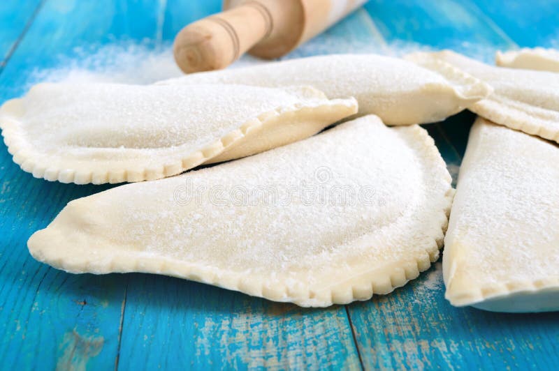 Not fried chebureks in flour on a blue wooden table. Traditional Turkic-Mongolian dish. Frozen semi-finished products. Not fried chebureks in flour on a blue wooden table. Traditional Turkic-Mongolian dish. Frozen semi-finished products.