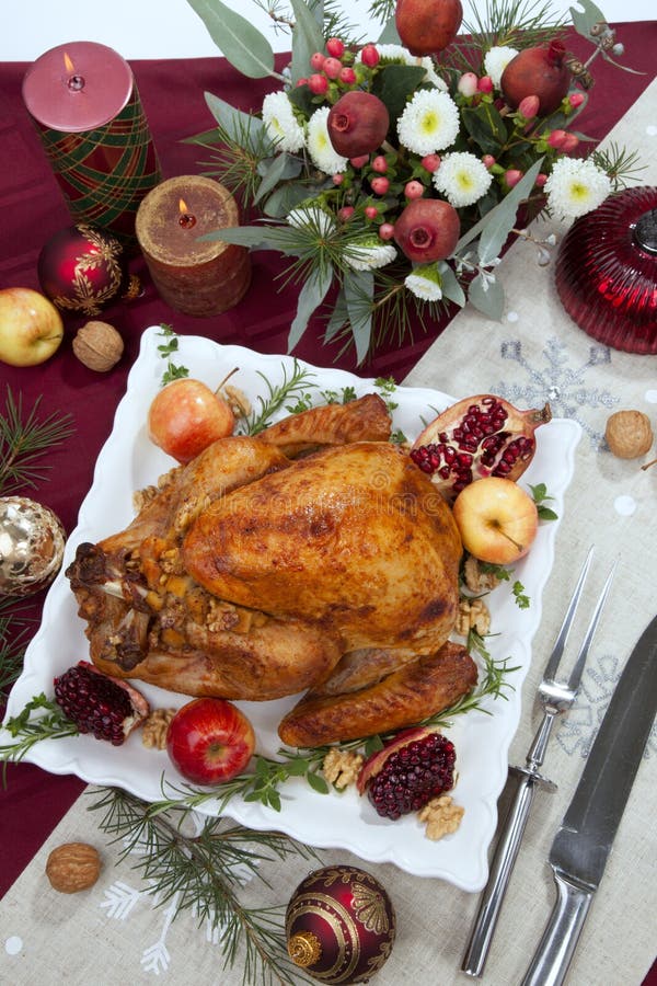 Pomegranate glazed roasted turkey on a tray garnished with fresh pomegranates, apples, herbs, and walnuts on Christmas-decorated table with candles, ornaments, fir twigs and flutes of champagne. Pomegranate glazed roasted turkey on a tray garnished with fresh pomegranates, apples, herbs, and walnuts on Christmas-decorated table with candles, ornaments, fir twigs and flutes of champagne