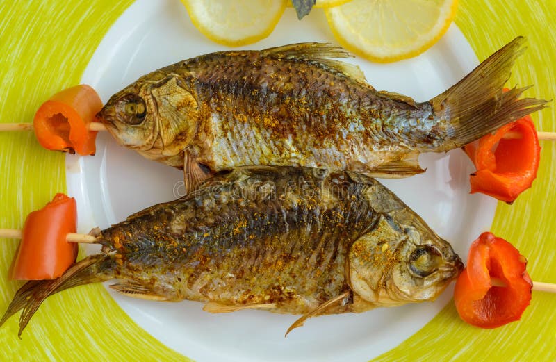 Gebratene Fische u. x28; carp& x29; auf Aufsteckspindeln mit Stücken Pfeffer und Zitrone Die Draufsicht stockfotos