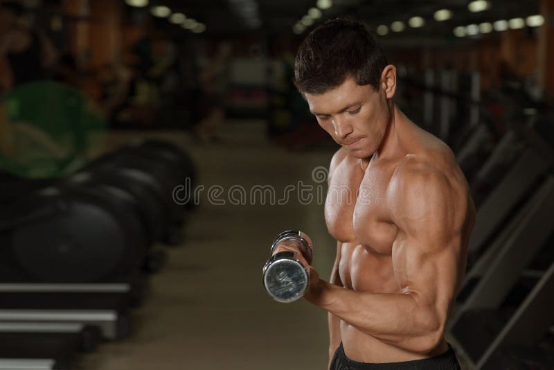 Gebräuntes muskulöses Manntraining mit Dummköpfen in der Turnhalle stockbild Gebräuntes muskulöses Manntraining mit Dummköpfen in der Turnhalle stockbild