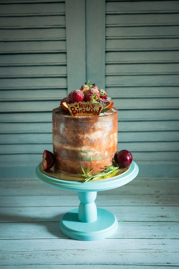 Geburtstagskuchen mit Erdbeere. Nahaufnahme von Weiß und Braun backt verziert mit Erdbeere und Pflaume zusammen Stände auf blauem hölzernem Sockel mit Zweig des Rosmarins und des alles Gute zum Geburtstag unterzeichnen