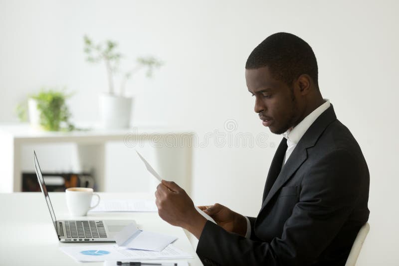 Serious African American CEO attentively reading received letter, business person analyzing offer or job promotion, getting to know company financial stats news, analyzing risks. Serious African American CEO attentively reading received letter, business person analyzing offer or job promotion, getting to know company financial stats news, analyzing risks