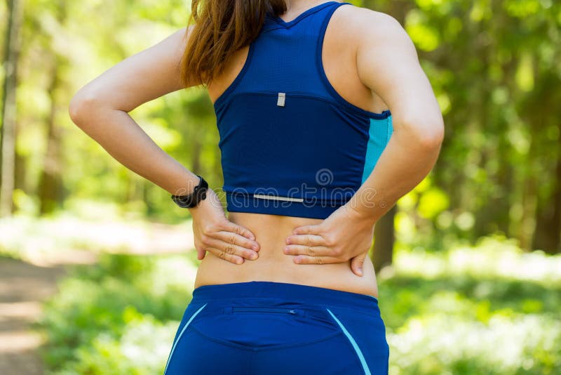 Close up athletic woman with smartwatches holding her painful injured back while doing an exercise. Close up athletic woman with smartwatches holding her painful injured back while doing an exercise.