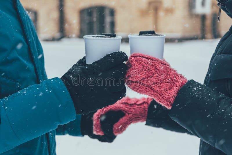 partial view of couple with hot drinks holding hands on street in winter. partial view of couple with hot drinks holding hands on street in winter