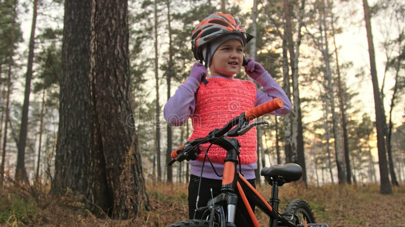Gedekte helm Eén kaukasische kinderfietsweg in het herfstpark Klein meisje met zwarte oranje cyclus in het bos