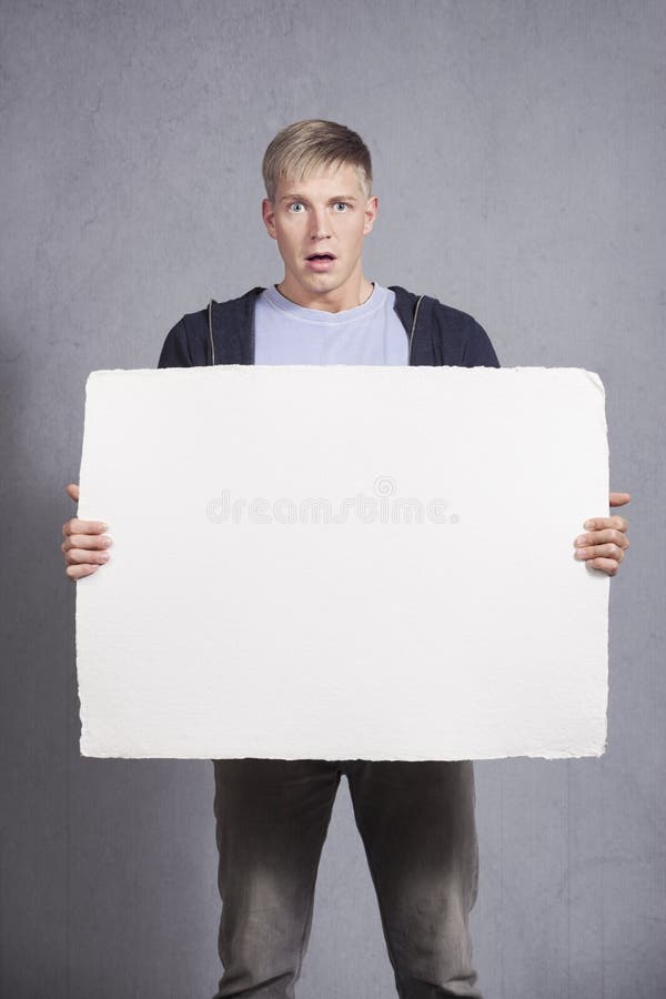 Upsetting news: Surprised man presenting white blank signboard with space for text isolated on grey background. Upsetting news: Surprised man presenting white blank signboard with space for text isolated on grey background.