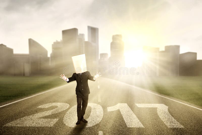 Image of a disoriented businessman walking on the road with number 2017 and cardboard head. Image of a disoriented businessman walking on the road with number 2017 and cardboard head