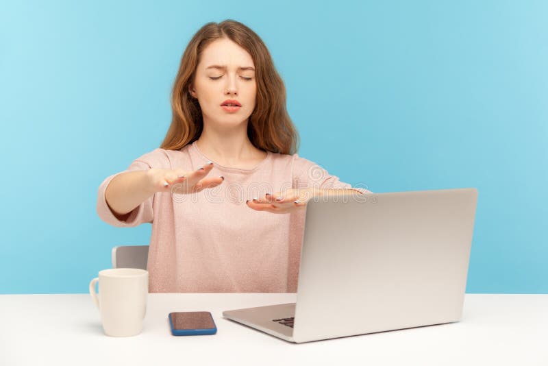 Disoriented blind young woman employee sitting at workplace with laptop and outstretching hands, touching air with attention to senses, having eyesight problems. indoor studio shot, blue background. Disoriented blind young woman employee sitting at workplace with laptop and outstretching hands, touching air with attention to senses, having eyesight problems. indoor studio shot, blue background