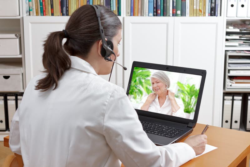 Doctor sitting at the desk of her office with headset and laptop, taking notes during a video call with a patient suffering from shoulder pain, telehealth or telemedicine concept. Doctor sitting at the desk of her office with headset and laptop, taking notes during a video call with a patient suffering from shoulder pain, telehealth or telemedicine concept