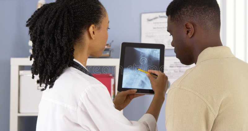 Geduldige Unterhaltung des Afroamerikaners mit Arzt über x-Strahlen auf Tablette lizenzfreie stockfotografie Geduldige Unterhaltung des Afroamerikaners mit Arzt über x-Strahlen auf Tablette lizenzfreie stockfotografie