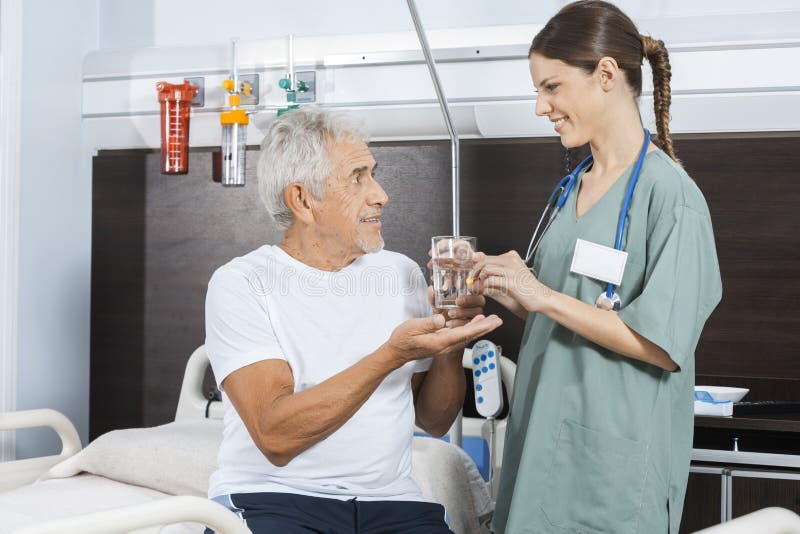 Geduldiges empfangendes Wasser-Glas und Pille von der weiblichen Krankenschwester stockfotografie Geduldiges empfangendes Wasser-Glas und Pille von der weiblichen Krankenschwester stockfotografie