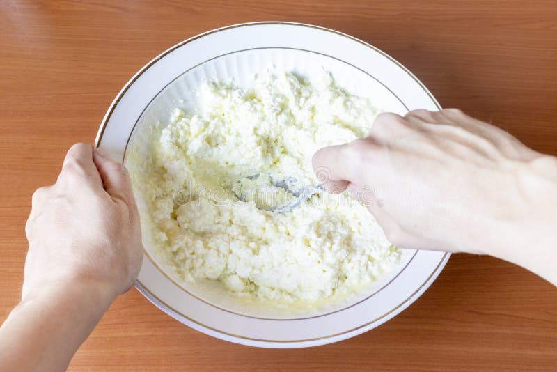 Geerntete weibliche Hände mischen Hüttenkäse in einer Schüssel lizenzfreie stockbilder Geerntete weibliche Hände mischen Hüttenkäse in einer Schüssel lizenzfreie stockbilder