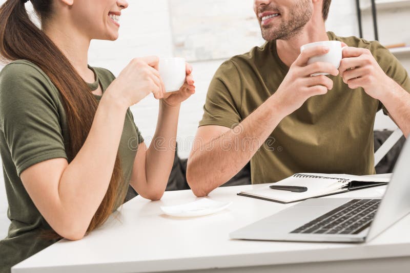 Geernteter Schuss des trinkenden Kaffees und mit Laptop zusammenarbeiten des glücklichen Paars stockfotografie