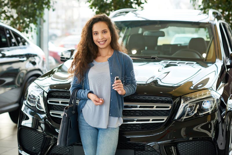 Portrait shot of attractive mixed race woman looking at camera with charming smile after buying car of her dream, interior of modern showroom on background. Portrait shot of attractive mixed race woman looking at camera with charming smile after buying car of her dream, interior of modern showroom on background