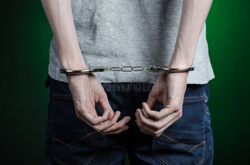Gefängnis und überführtes Thema: Mann mit den Handschellen auf seinen Händen in einem grauen T-Shirt und in den Blue Jeans auf ei lizenzfreie stockfotografie Gefängnis und überführtes Thema: Mann mit den Handschellen auf seinen Händen in einem grauen T-Shirt und in den Blue Jeans auf ei lizenzfreie stockfotografie