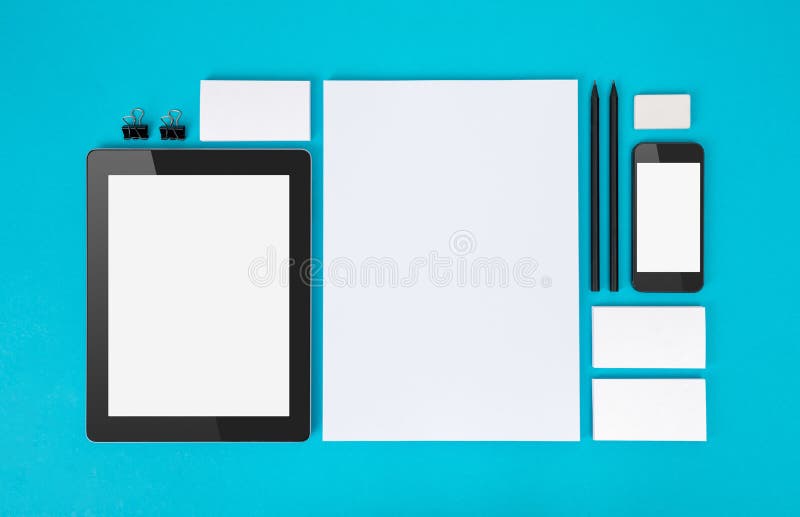 Set of variety blank office objects organized for company presentation or branding identity with blank modern devices. Isolated on blue paper background. Set of variety blank office objects organized for company presentation or branding identity with blank modern devices. Isolated on blue paper background.