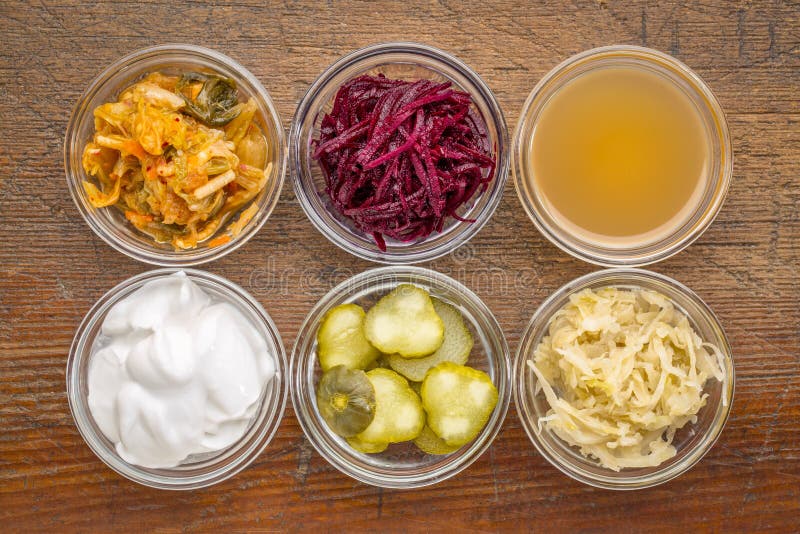 A set of fermented food great for gut health - top view of glass bowls against rustic wood: kimchi, red beets, apple cider vinegar, coconut milk yogurt, cucumber pickles, sauerkraut. A set of fermented food great for gut health - top view of glass bowls against rustic wood: kimchi, red beets, apple cider vinegar, coconut milk yogurt, cucumber pickles, sauerkraut