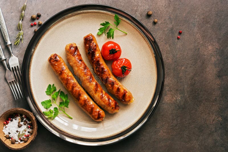 Gegrillte W?rste auf einer Platte mit Kirschtomaten, brauner rustikaler Hintergrund Obenliegende Ansicht, Kopienraum stockbild Gegrillte W?rste auf einer Platte mit Kirschtomaten, brauner rustikaler Hintergrund Obenliegende Ansicht, Kopienraum stockbild
