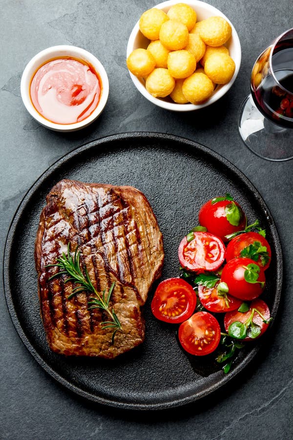 Gegrilltes Rindfleischsteak diente auf Roheisenplatte mit Tomatensalat, Kartoffelbällen und Rotwein Grill, bbq-Fleischrindfleisch lizenzfreies stockfoto Gegrilltes Rindfleischsteak diente auf Roheisenplatte mit Tomatensalat, Kartoffelbällen und Rotwein Grill, bbq-Fleischrindfleisch lizenzfreies stockfoto