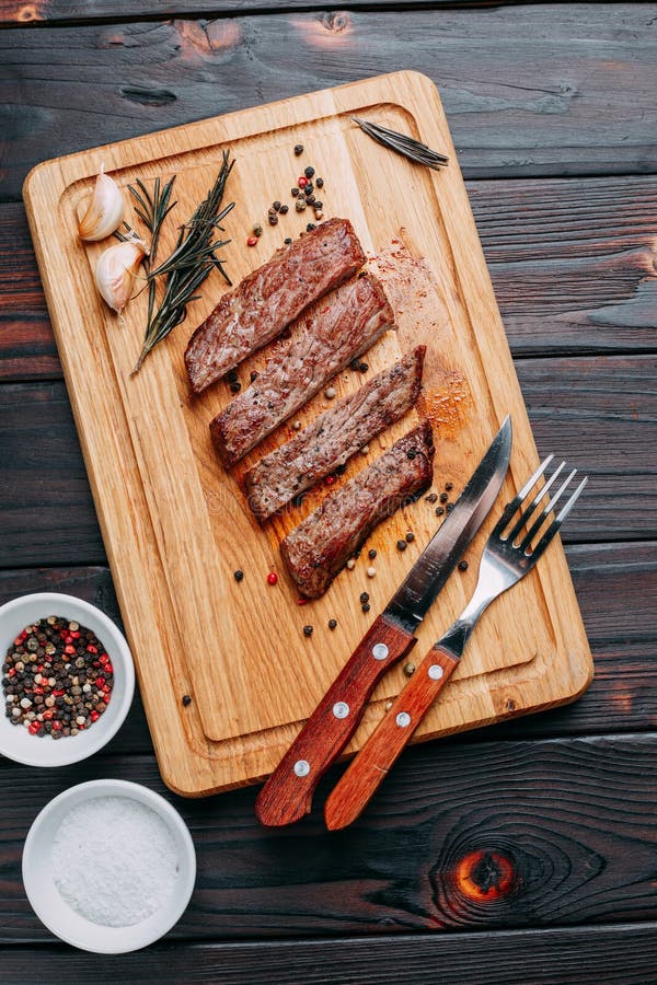 Gegrilltes Rindfleischsteak mit Kräutern und Gewürzen auf Schneidebrett und Cu lizenzfreies stockbild Gegrilltes Rindfleischsteak mit Kräutern und Gewürzen auf Schneidebrett und Cu lizenzfreies stockbild