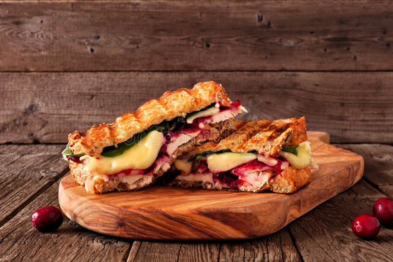 Gegrilltes Truthahn-, Moosbeer- und Briekäsesandwich auf einem dienenden Board gegen dunkles Holz stockbild