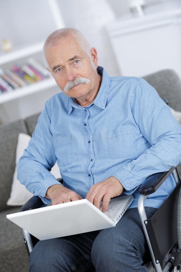 Gehandicapte hogere mensenzitting in rolstoel die laptop met behulp van royalty-vrije stock foto Gehandicapte hogere mensenzitting in rolstoel die laptop met behulp van royalty-vrije stock foto