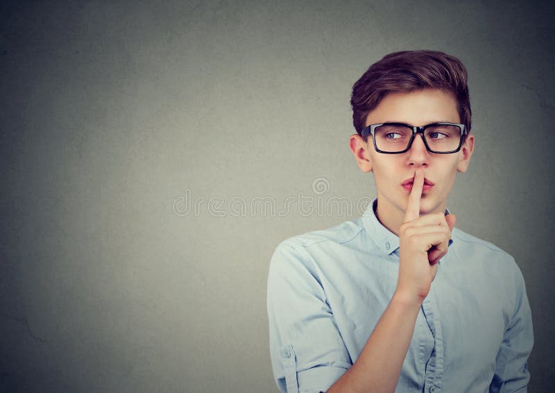 Secret guy. Man saying hush be quiet with finger on lips gesture looking to the side isolated on gray wall background. Secret guy. Man saying hush be quiet with finger on lips gesture looking to the side isolated on gray wall background.