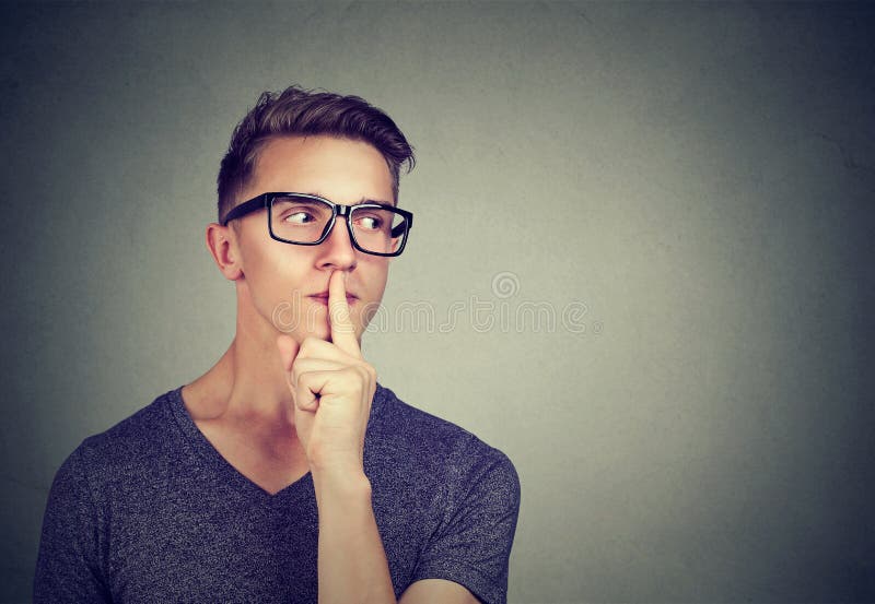 Secret guy. Man saying hush be quiet with finger on lips gesture looking to the side on gray wall background. Secret guy. Man saying hush be quiet with finger on lips gesture looking to the side on gray wall background.