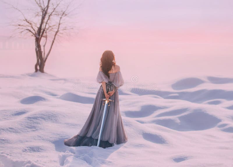 Geheimzinnige dame van Middeleeuwen met donker haar in zachte grijze blauwe kleding in sneeuwwoestijn met open rug en schouders