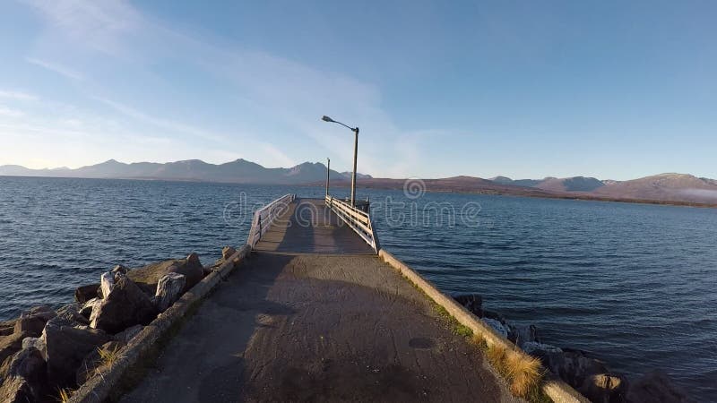 Gehen auf langen geraden Pier im hellen Sonnenschein mit Gebirgs- und Fjordhintergrund