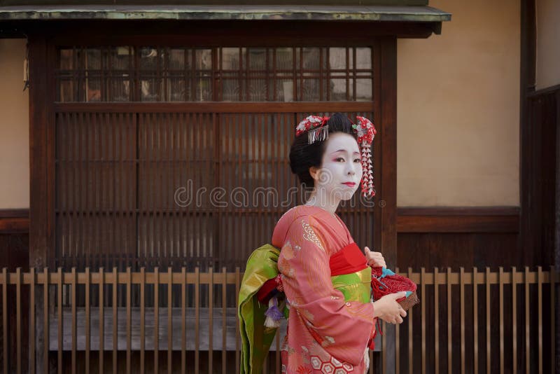 Geisha o maiko en un kimono que camina delante de la puerta de un tradicional fotos de archivo Geisha o maiko en un kimono que camina delante de la puerta de un tradicional fotos de archivo