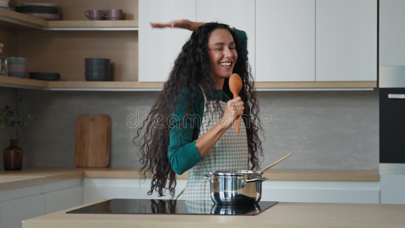 Gekke energetische artistieke vrouw die alleen plezier heeft in de keuken neemt muzikale pauze als microfoon luid zingen