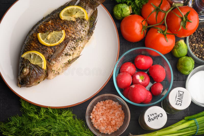 Gekookte vis met citroen, op een zwarte houten achtergrond, met ingrediënten en groenten Fantastisch en gezond voedsel