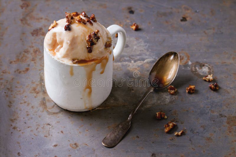 Vintage ceramic cup with homemade caramel and Hazelnut butter Ice cream, served with caramel syrup and crispy nuts over rusty metal textured background. Vintage ceramic cup with homemade caramel and Hazelnut butter Ice cream, served with caramel syrup and crispy nuts over rusty metal textured background.