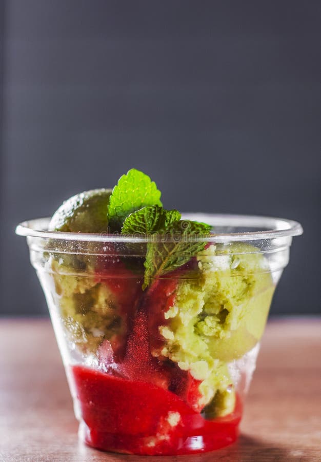 Gelato dell'avocado e sorbetto organici verdi della fragola con vino rosso in una tazza di plastica con la menta immagini stock libere da diritti Gelato dell'avocado e sorbetto organici verdi della fragola con vino rosso in una tazza di plastica con la menta immagini stock libere da diritti