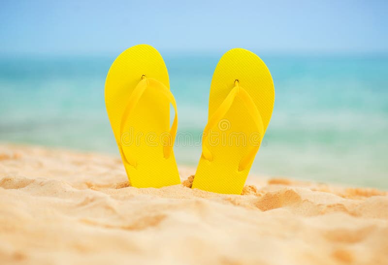 Yellow sandal flip flop on the white sand beach with blue sea and sky background in summer vacations copy space. Yellow sandal flip flop on the white sand beach with blue sea and sky background in summer vacations copy space.