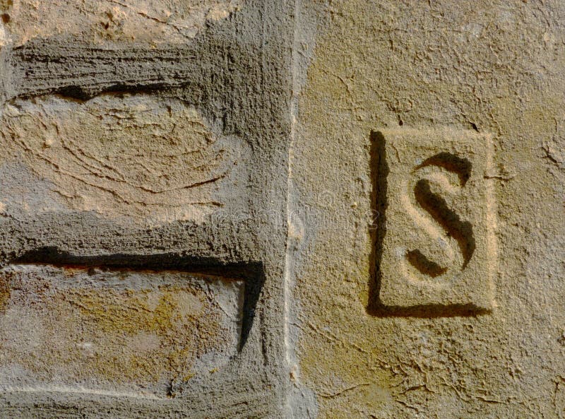 Yellow brick macro closeup of special stamped brick with letter S. rough clay sandy and gritty texture.  construction industry and architecture concept. exposed brick fence detail with strong shadow. proud cement mortar joint. brushed texture. Yellow brick macro closeup of special stamped brick with letter S. rough clay sandy and gritty texture.  construction industry and architecture concept. exposed brick fence detail with strong shadow. proud cement mortar joint. brushed texture.