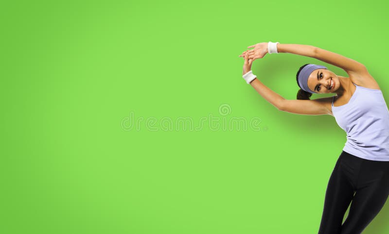 Happy smiling african american woman in grey sportswear doing stretching exercise or youga moves, isolated over green background. Young sporty model at studio. Health, beauty and fitness concept. Happy smiling african american woman in grey sportswear doing stretching exercise or youga moves, isolated over green background. Young sporty model at studio. Health, beauty and fitness concept