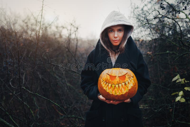 Gelukkig Halloween-Portret van zwarte moderne levensstijlheks in kap en zwarte laagmantel op houten struik bosachtergrond royalty-vrije stock fotografie Gelukkig Halloween-Portret van zwarte moderne levensstijlheks in kap en zwarte laagmantel op houten struik bosachtergrond royalty-vrije stock fotografie