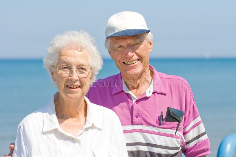 A happy and smiling senior couple with his arm around her standing in front of a large lake while on vacation. A happy and smiling senior couple with his arm around her standing in front of a large lake while on vacation.