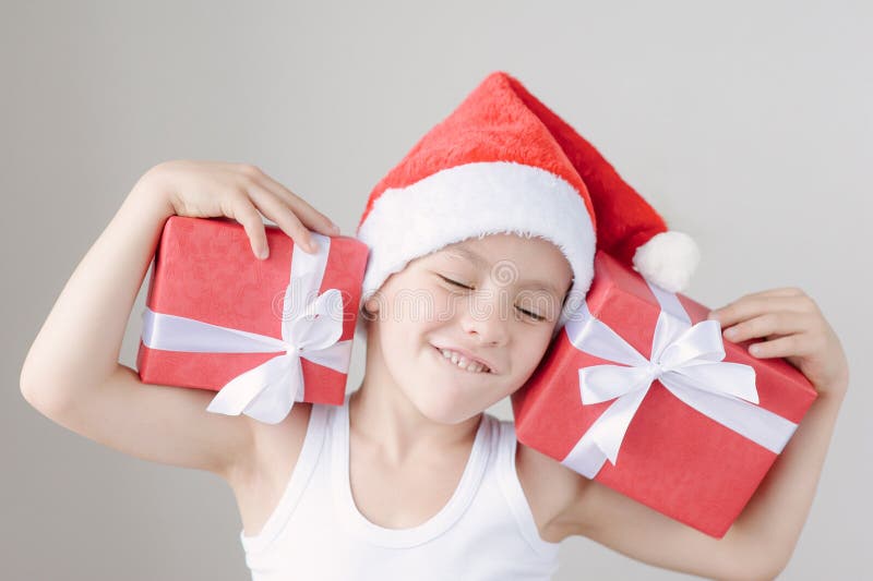 Gelukkig houdt weinig jongen in Kerstman` s hoed en t-shirt dozen van giften stock foto Gelukkig houdt weinig jongen in Kerstman` s hoed en t-shirt dozen van giften stock foto