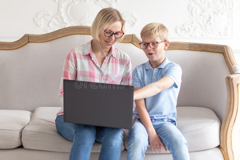 Gelukkig jong mamma en haar zoonszitting op bank en het gebruiken van laptop Jonge jongen die iets tonen aan zijn mamma stock foto's Gelukkig jong mamma en haar zoonszitting op bank en het gebruiken van laptop Jonge jongen die iets tonen aan zijn mamma stock foto's