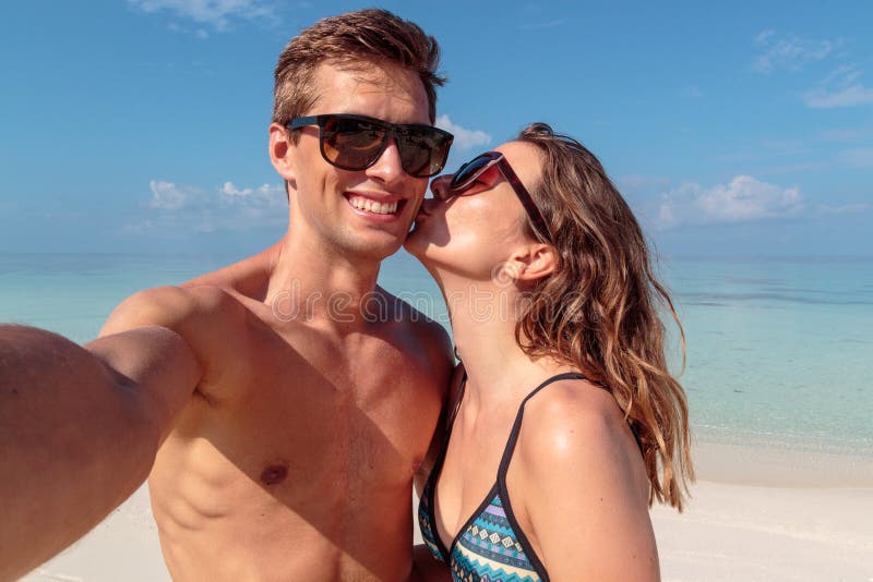 Gelukkig jong paar die een selfie, duidelijk blauw water als achtergrond nemen Meisje die zijn vriend kussen royalty-vrije stock foto's Gelukkig jong paar die een selfie, duidelijk blauw water als achtergrond nemen Meisje die zijn vriend kussen royalty-vrije stock foto's