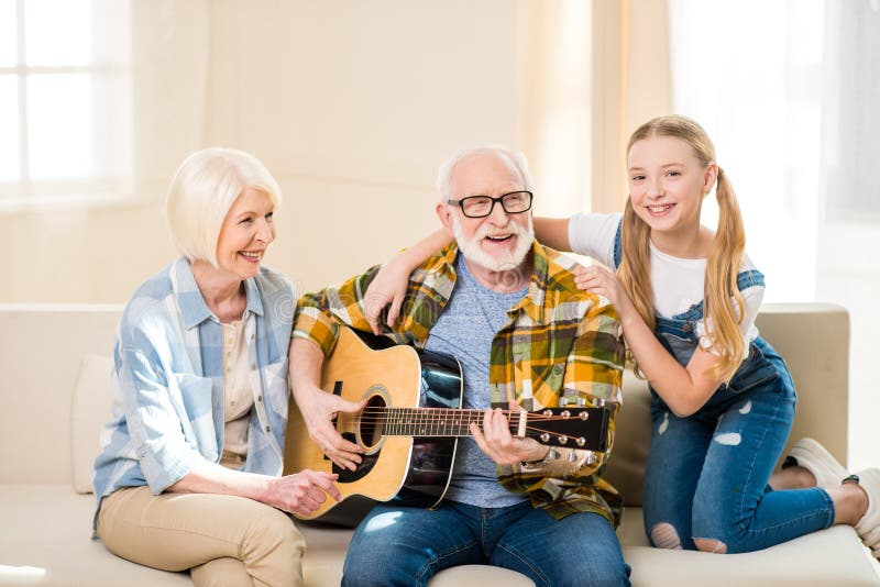 Gelukkig meisje met grootouders die samen op bank en het spelen akoestische gitaar zitten stock foto's Gelukkig meisje met grootouders die samen op bank en het spelen akoestische gitaar zitten stock foto's